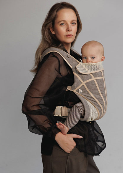 Partial view of Woman carrying baby on chest in a baby carrier. Woman is wearing black shirt and brown pants.
