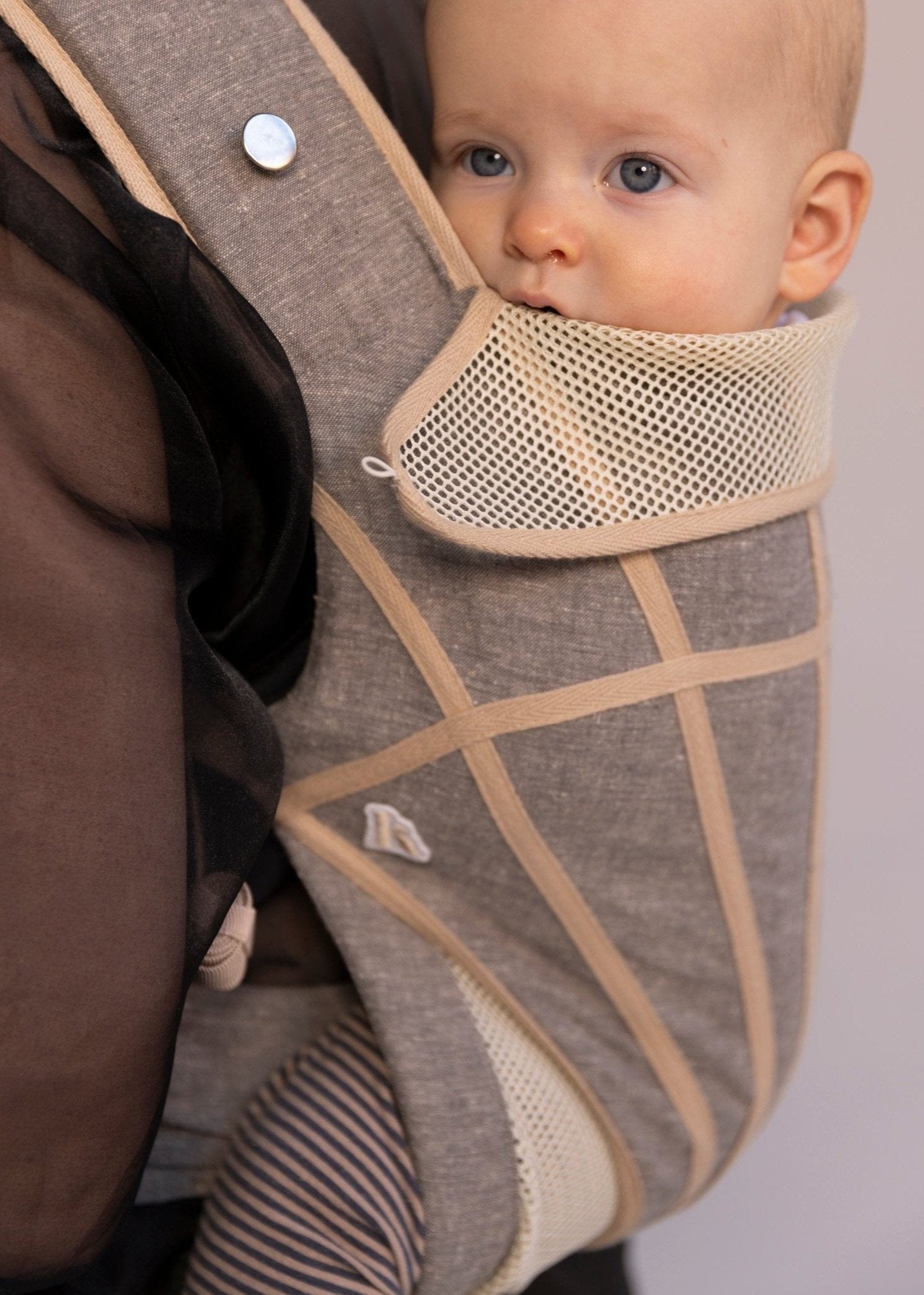 Closeup of baby in grey with tan stripes baby carrier.