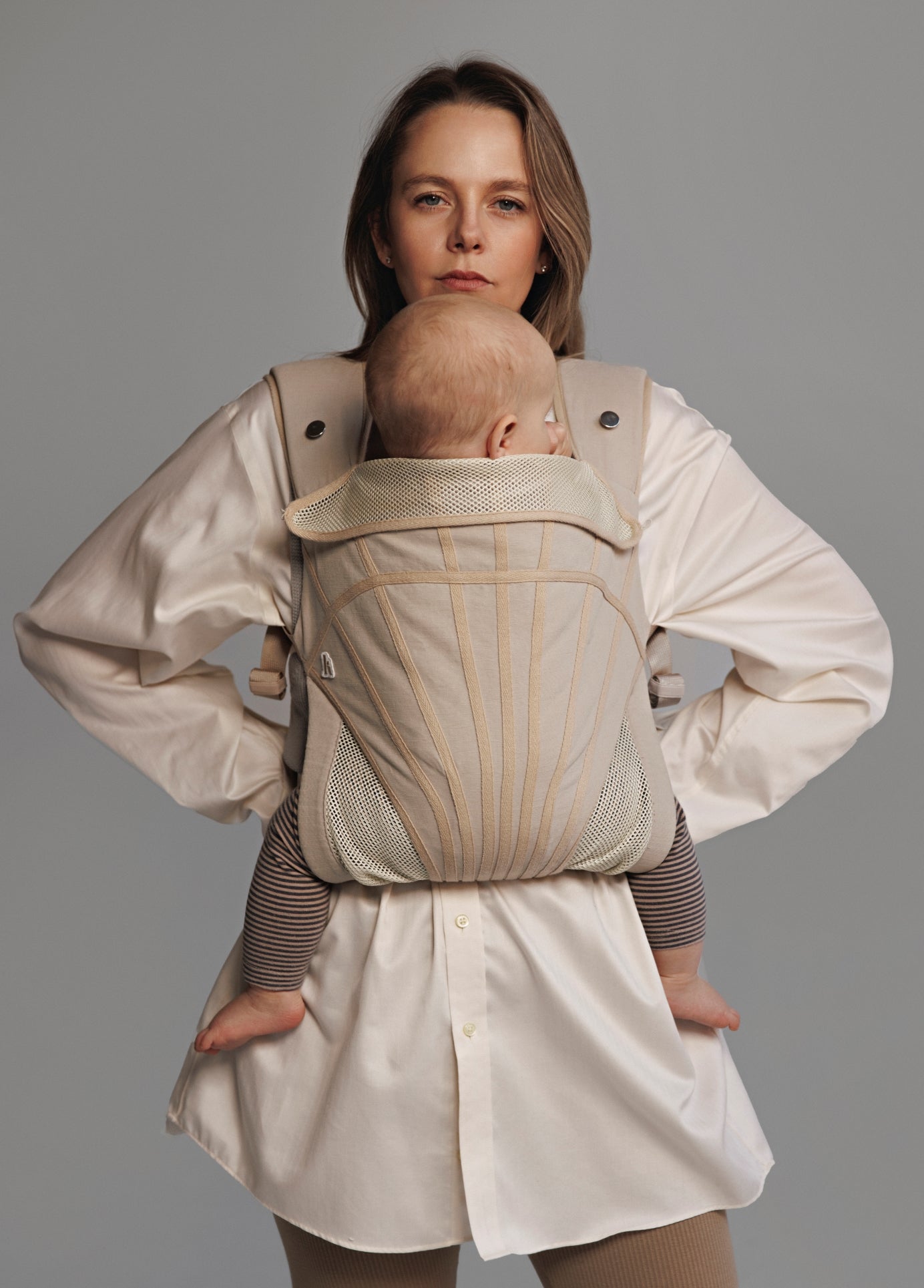 Woman carrying baby on chest in a baby carrier. Woman is wearing white shirt.