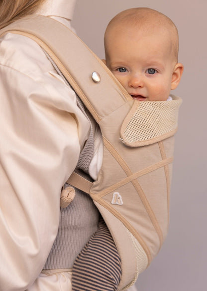 Closeup of cute baby in a baby carrier on the back of a woman.