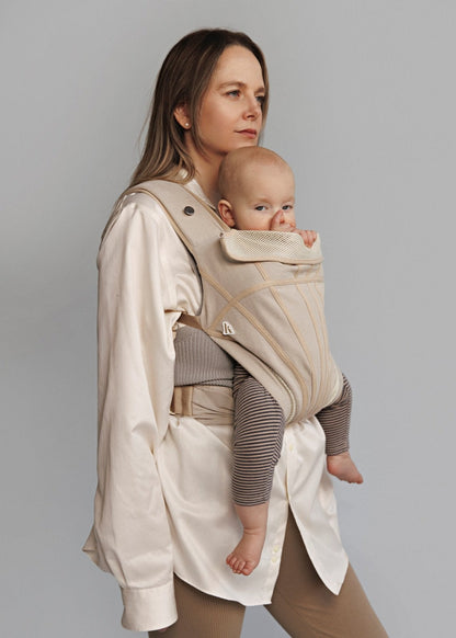 Partial front view of woman carrying baby on her front in a baby carrier. Woman is wearing white long shirt.