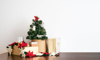 Felt poinsettia garland with alternating red and white flowers on boxes under tiny Christmas tree.