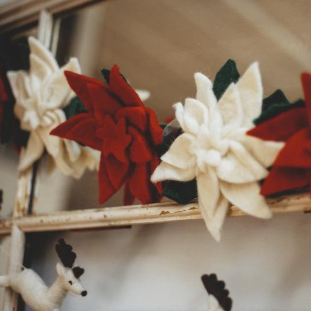 Felt poinsettia garland with alternating red and white flowers on a shelf.