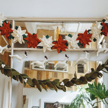 Felt poinsettia garland with alternating red and white flowers hanging with other holiday garlands.