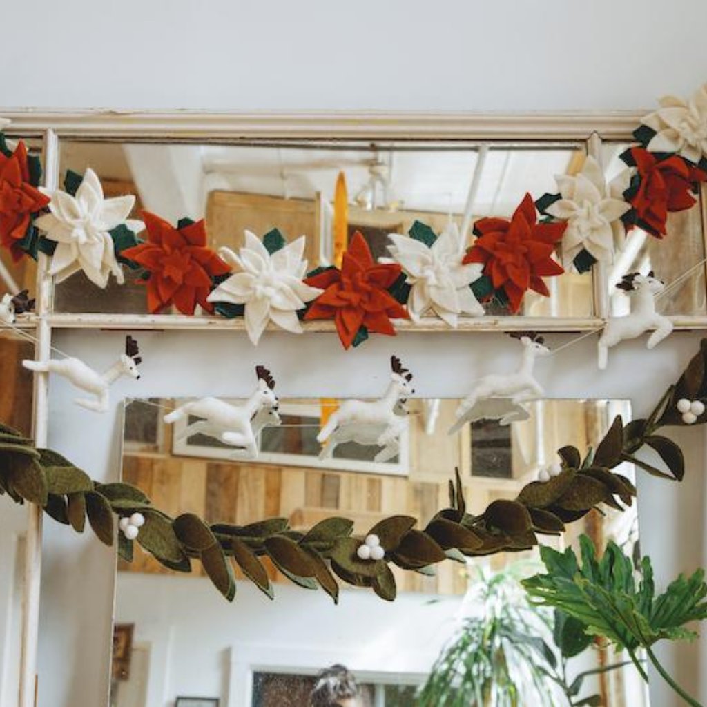 Felt garland red Santa and sleigh with white reindeer hanging with other Christmas garlands.