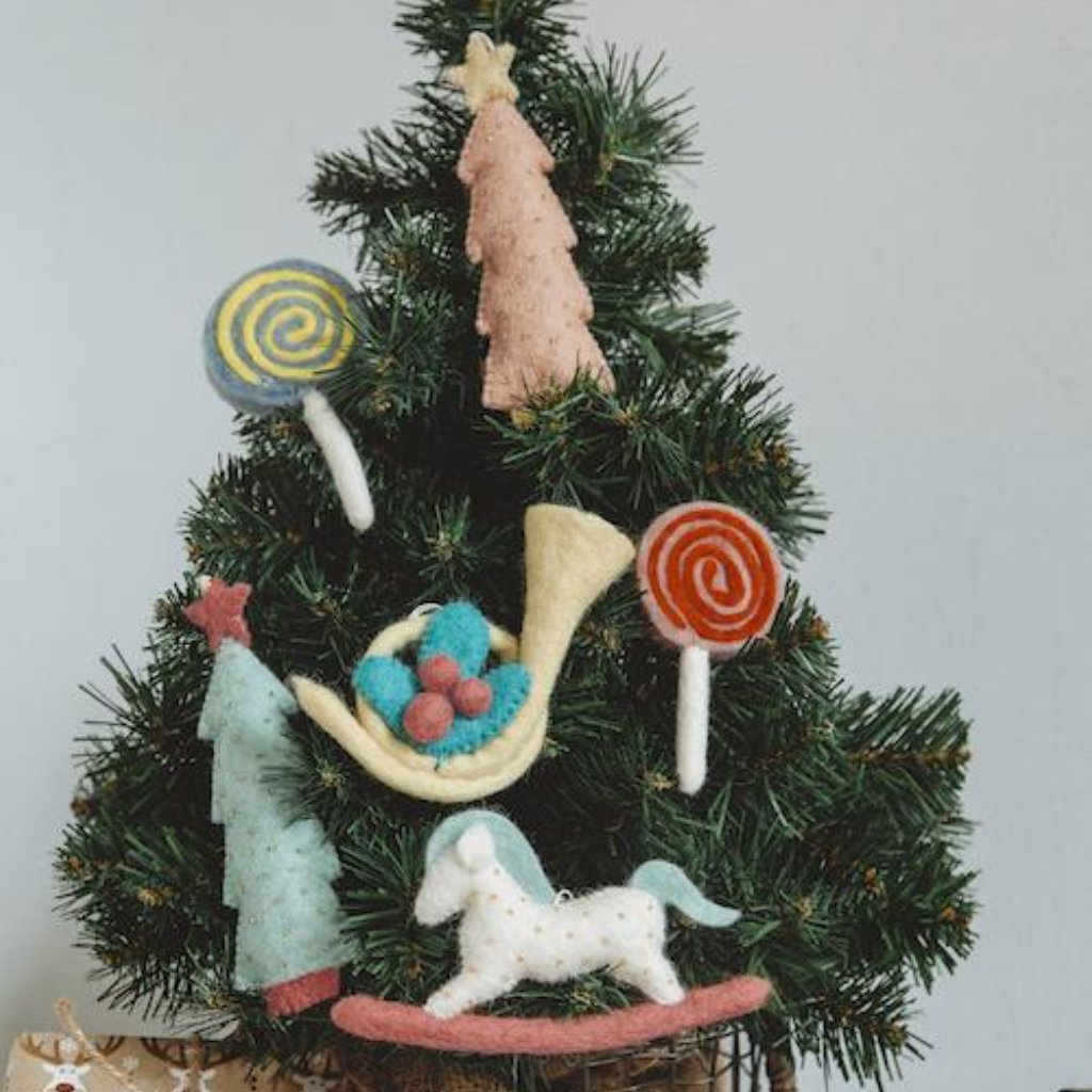 Felt ornament of a French Horn with a sprig of holly and berries with other various Nutcracker themed ornaments on a Christmas tree.