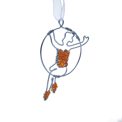 Wire and bead ornament of a woman swinging on a circus/aerial hoop in a red top and red shoes.