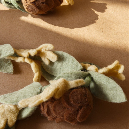 Close up of felt garland with green leaves and brown pinecones.