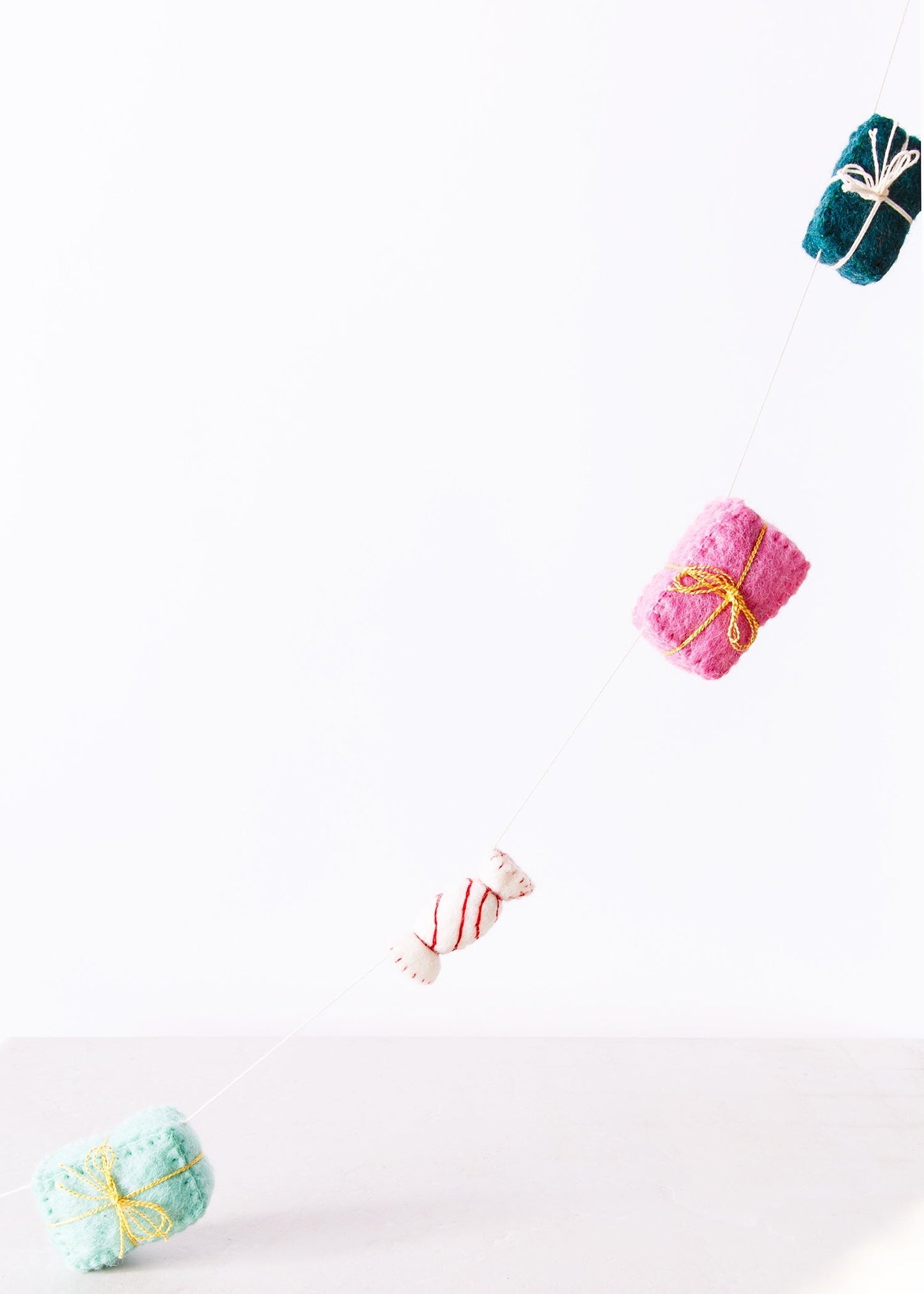 Felt garland of gifts in pink, teal, red, green and white hanging on wall.