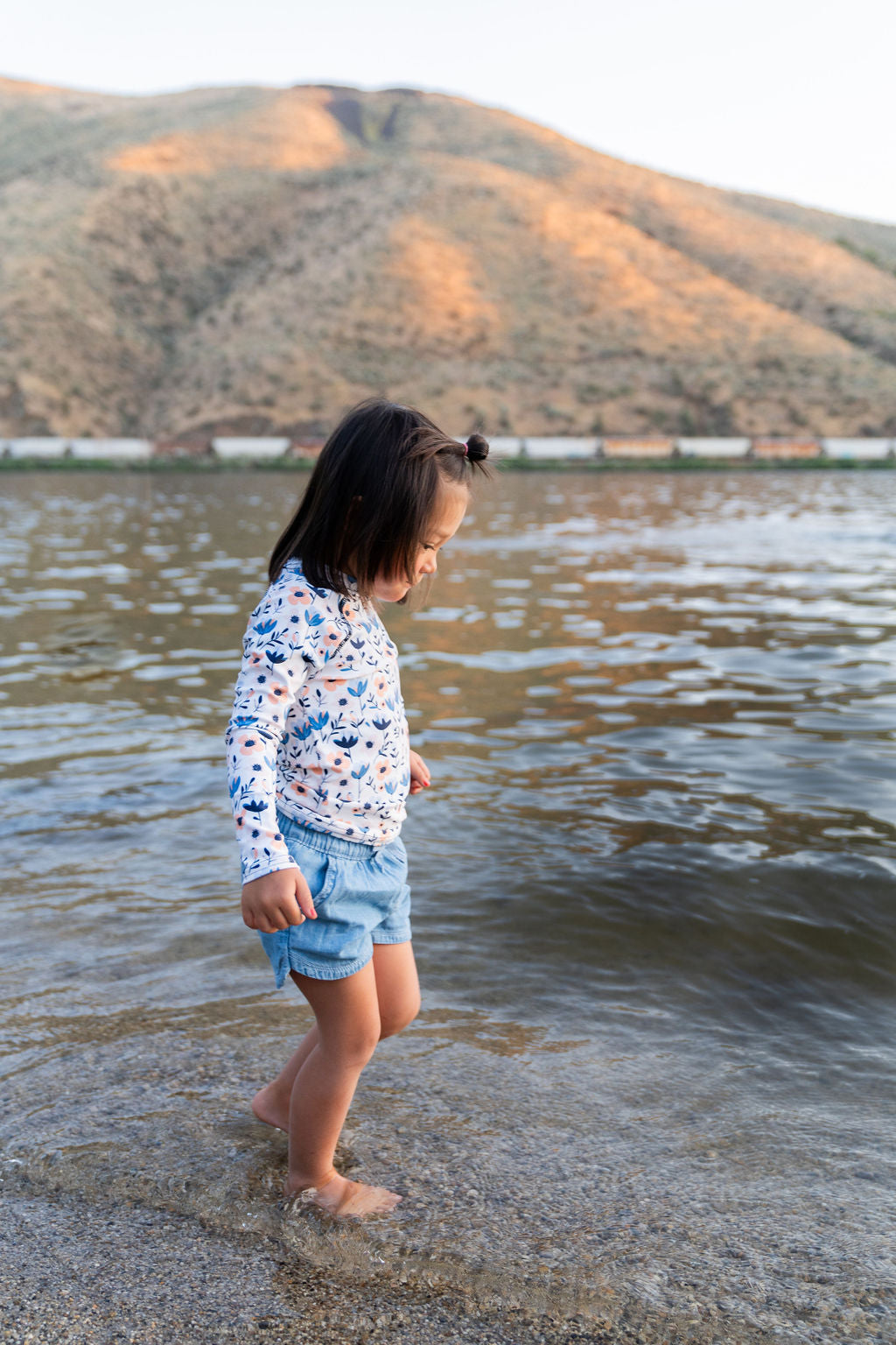 A girl stands by a stream, wearing a pastel floral bloom rash guard, combining comfort and style for her adventure.