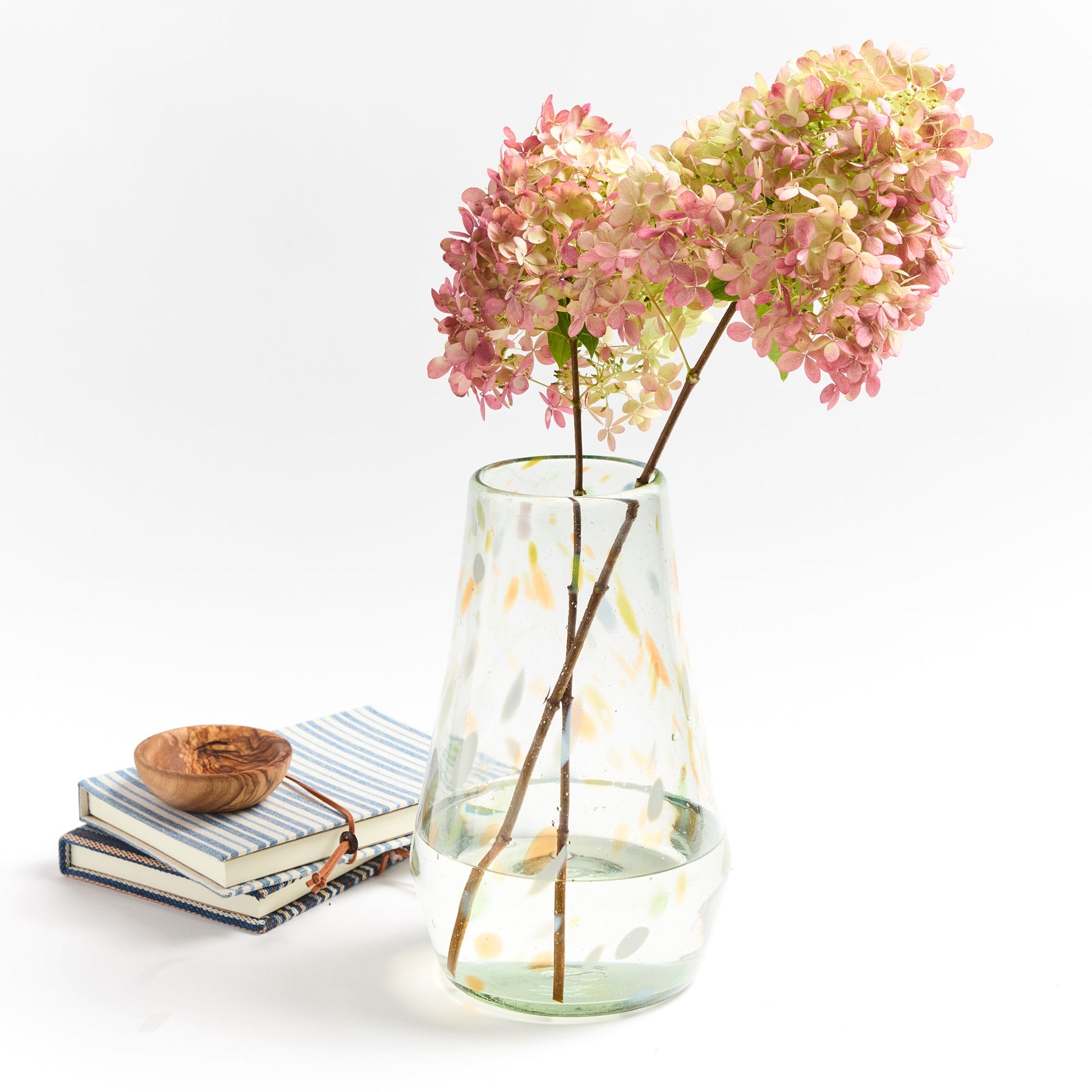 Clear vase with confetti markings of orange blue and green holding orange flowers.