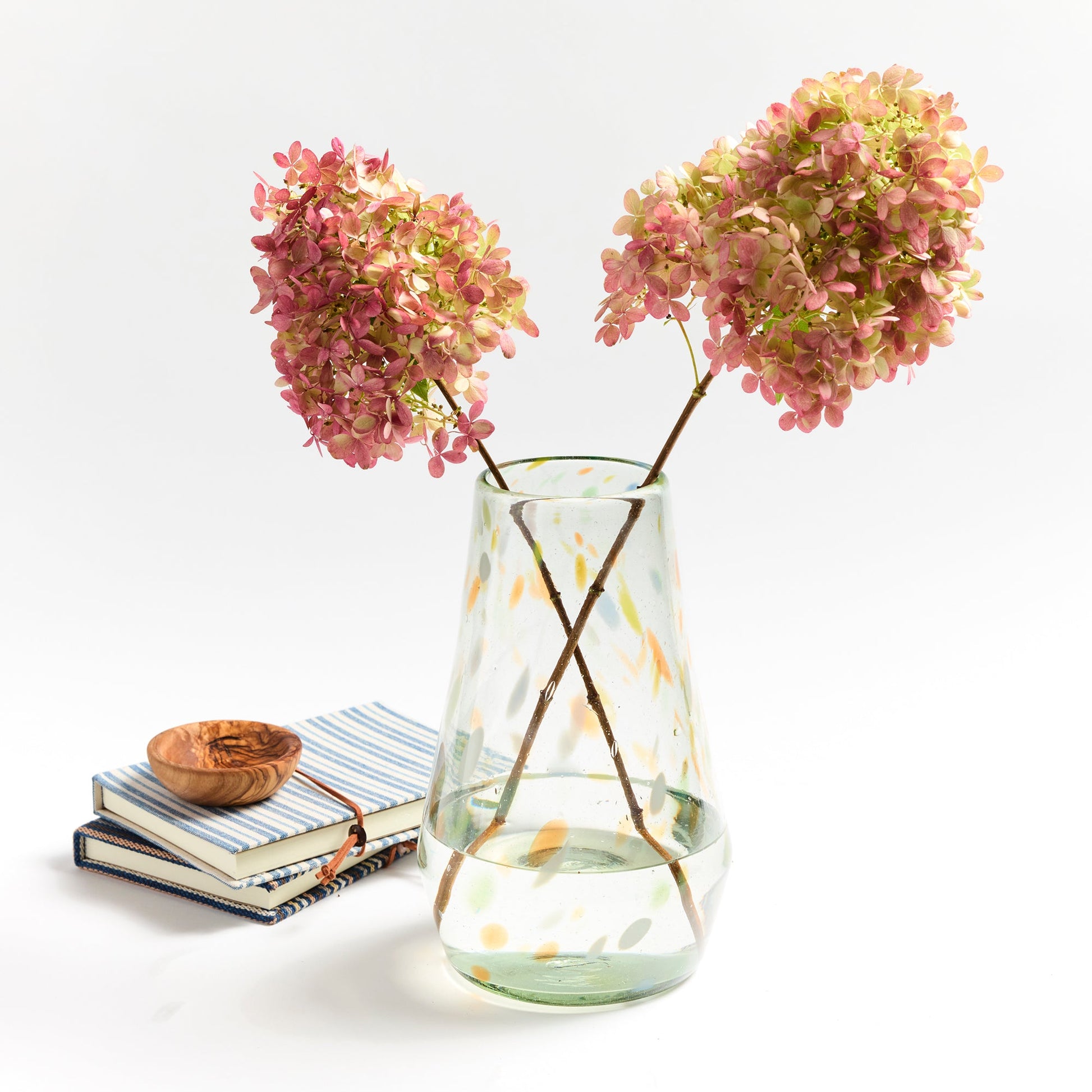 Clear vase with confetti markings of orange blue and green holding orange flowers.