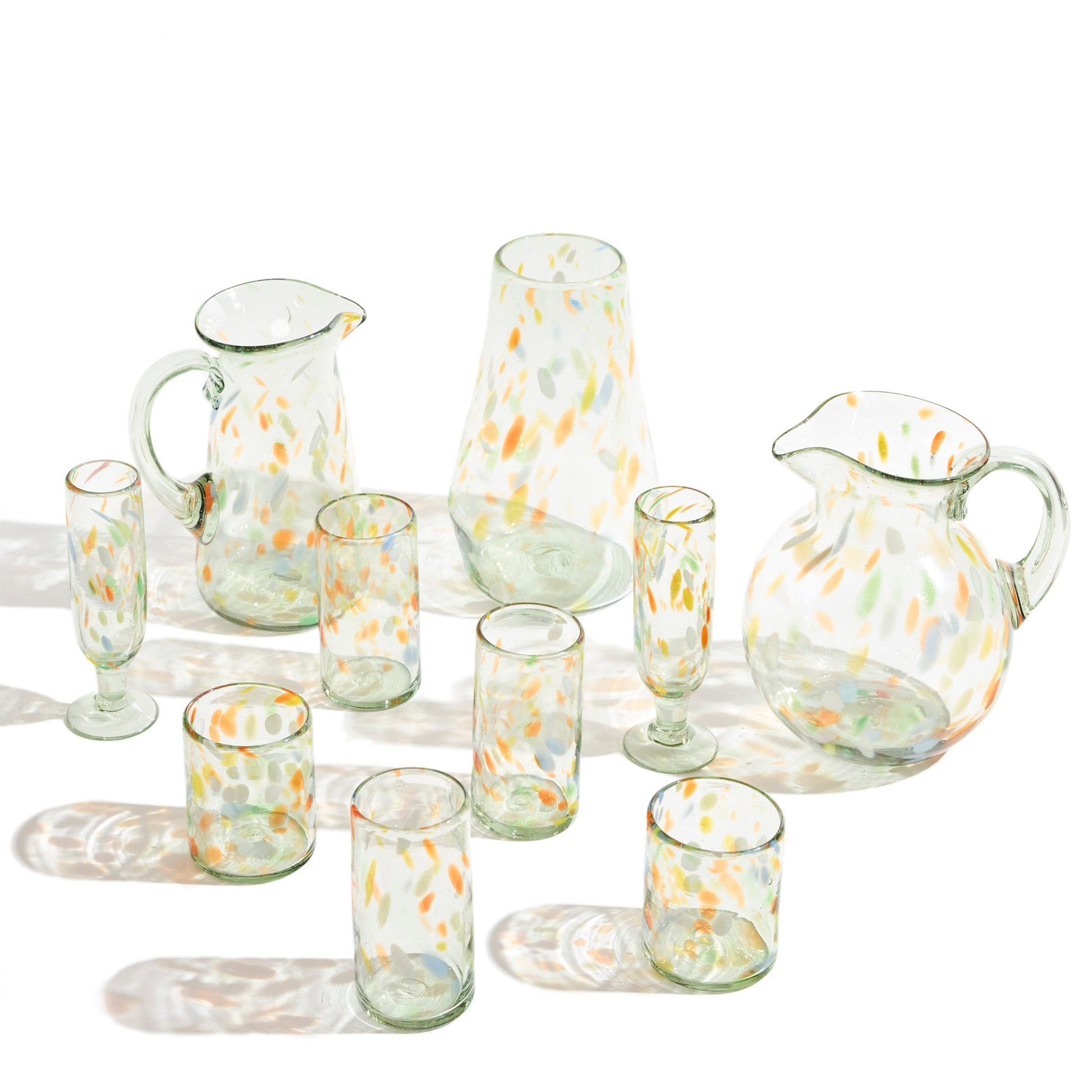 Clear vase with confetti markings of orange blue and green in a grouping of similar colored pitchers, vases, and glasses.