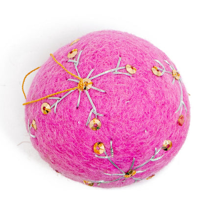 A round, bright pink felt ornament with white embroidery and gold sequin designs.