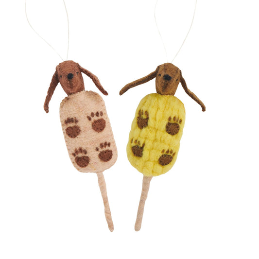 Felt ornaments of dogs, one in a brown corn dog on a stick and one in a yellow corn on a stick.