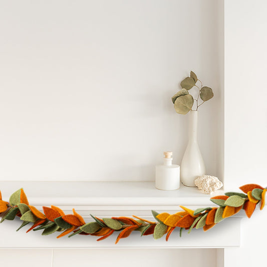 Felt garland of leaves in orange and green hanging from white mantel.
