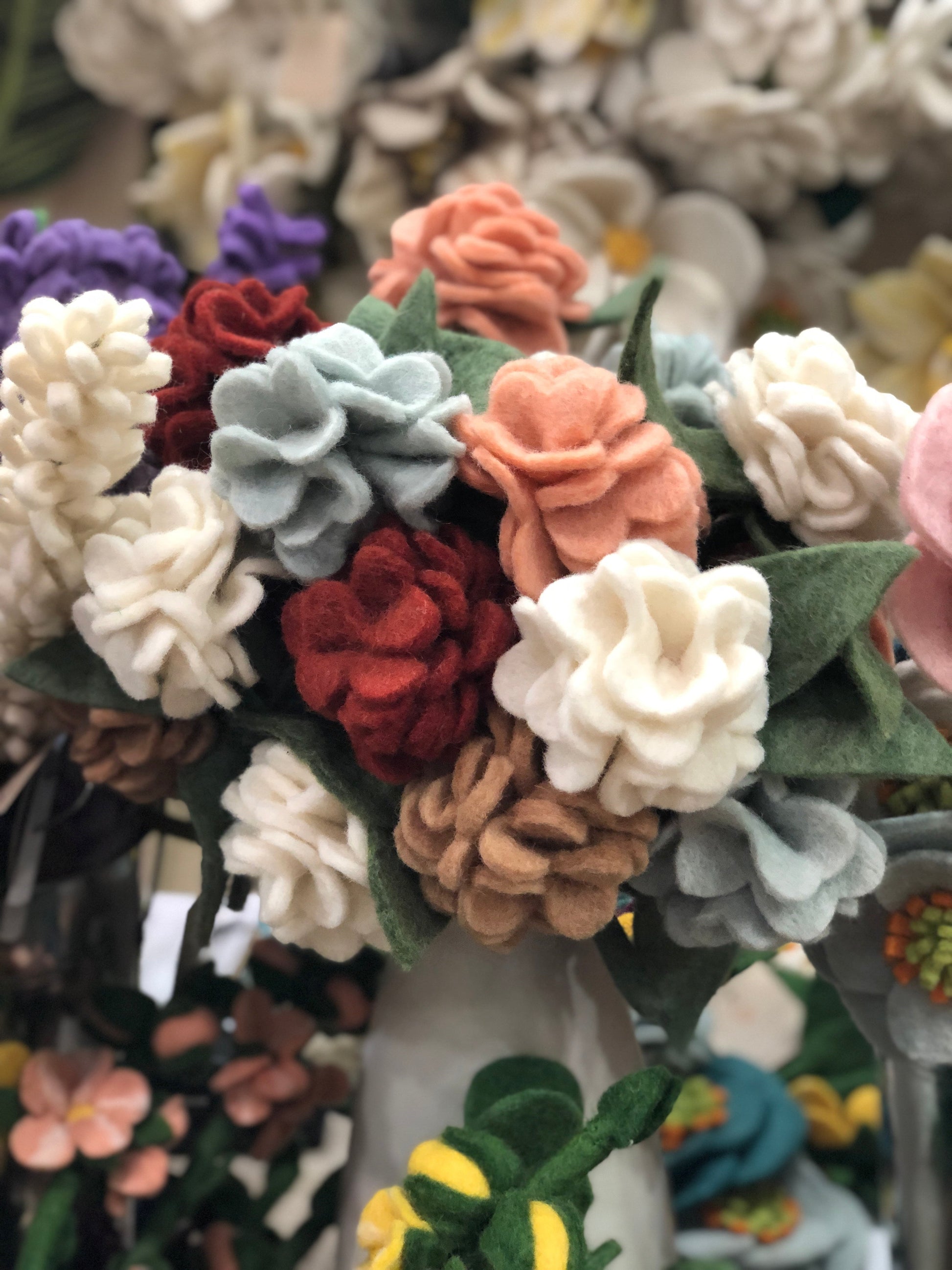 White, tan, pink, red, and light blue felt Geranium flowers in white vase.