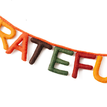 Close up of felt garland spelling out Grateful and Full each letter in different colors of red, yellow, orange, brown, and green.