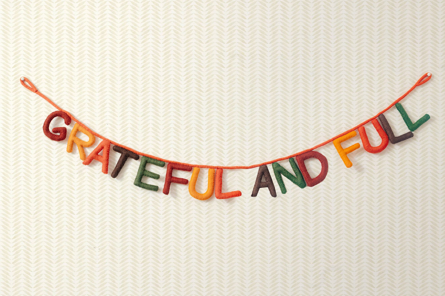 Hanging felt garland spelling out Grateful and Full each letter in different colors of red, yellow, orange, brown, and green.