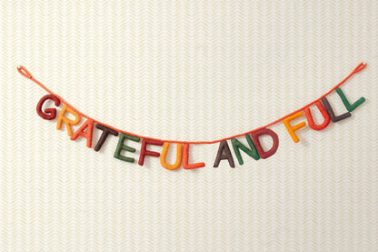 Hanging felt garland spelling out Grateful and Full each letter in different colors of red, yellow, orange, brown, and green.