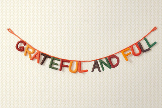 Hanging felt garland spelling out Grateful and Full each letter in different colors of red, yellow, orange, brown, and green.