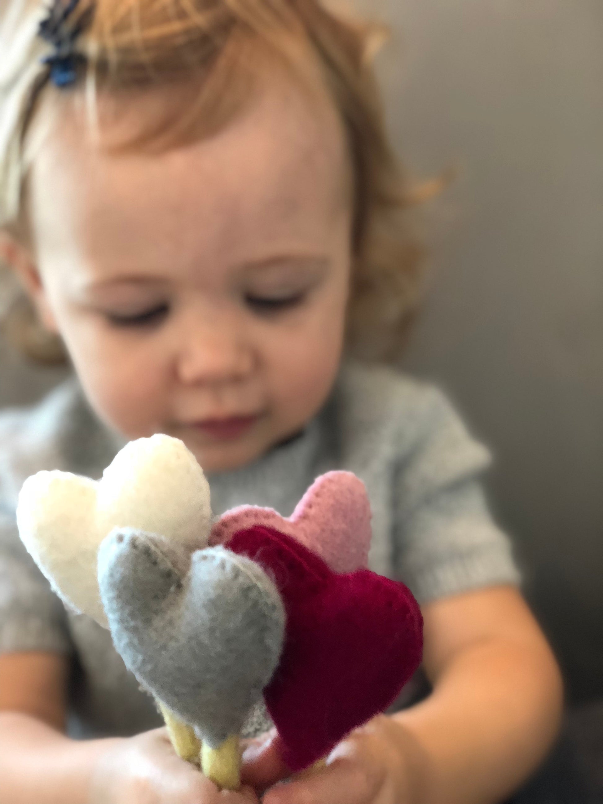 Felt heart accent stems in white, pink, blue, and red shown being held by baby in blue dress.