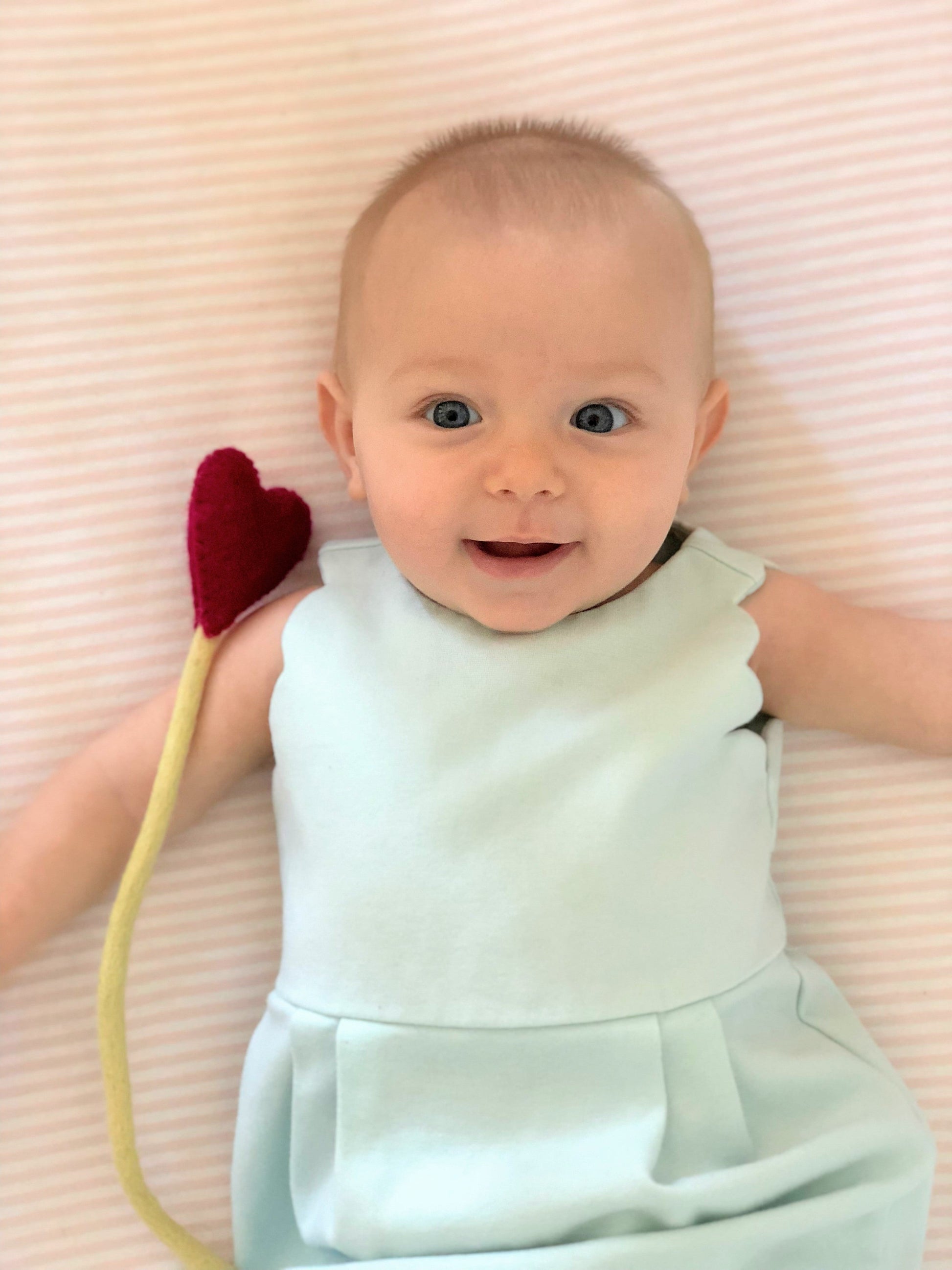 Felt heart accent stem in red shown being held by baby in blue dress.