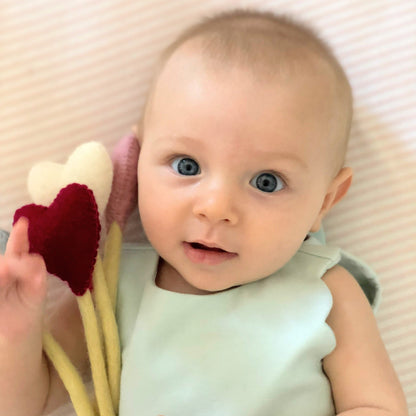 Felt heart accent stems in white, pink, blue, and red shown being held by baby in blue dress.