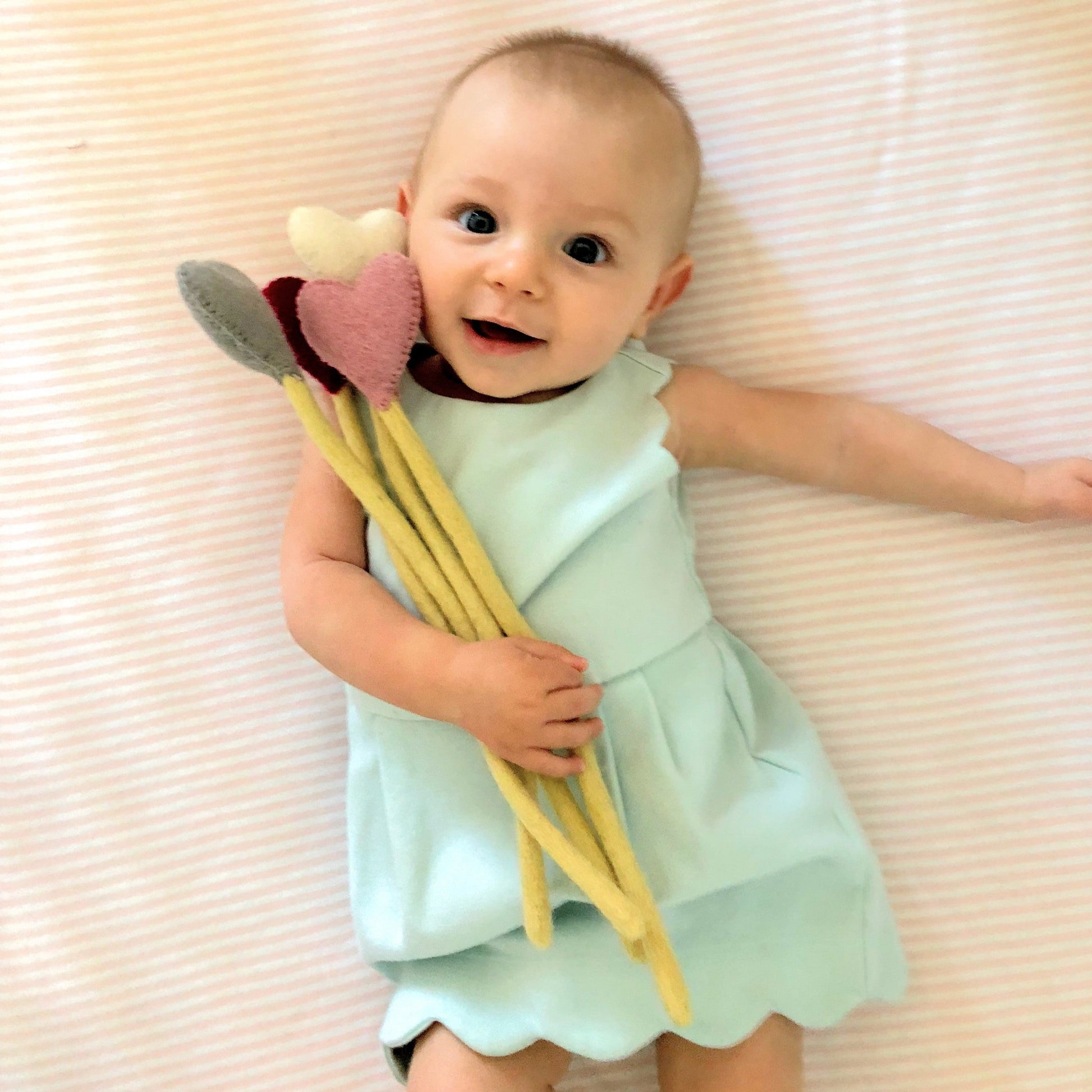 Felt heart accent stems in white, pink, blue, and red shown being held by baby in blue dress.