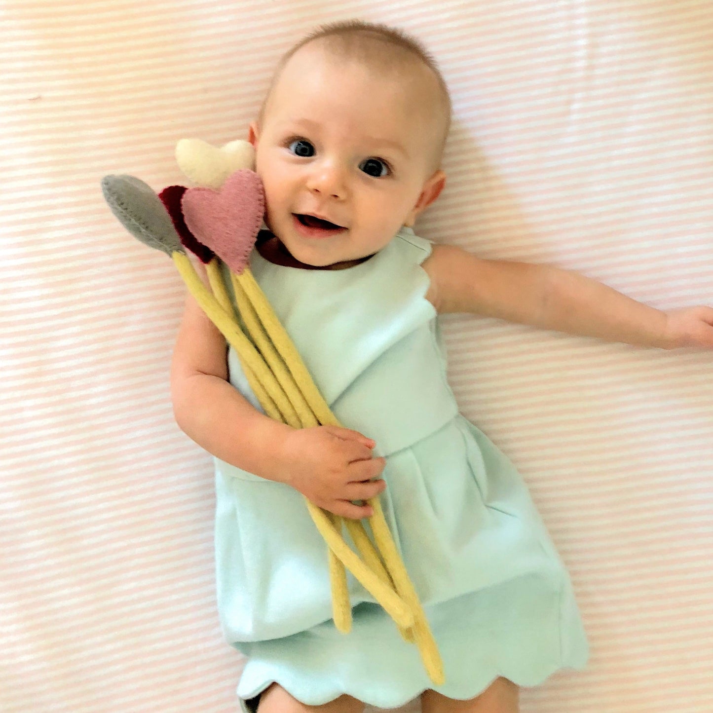 Felt heart accent stems in white, pink, blue, and red shown being held by baby in blue dress.
