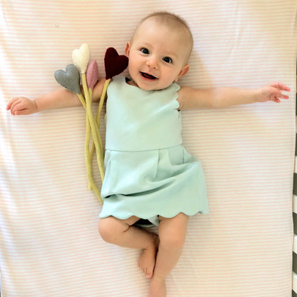 Felt heart accent stems in white, pink, blue, and red shown being held by baby in blue dress.