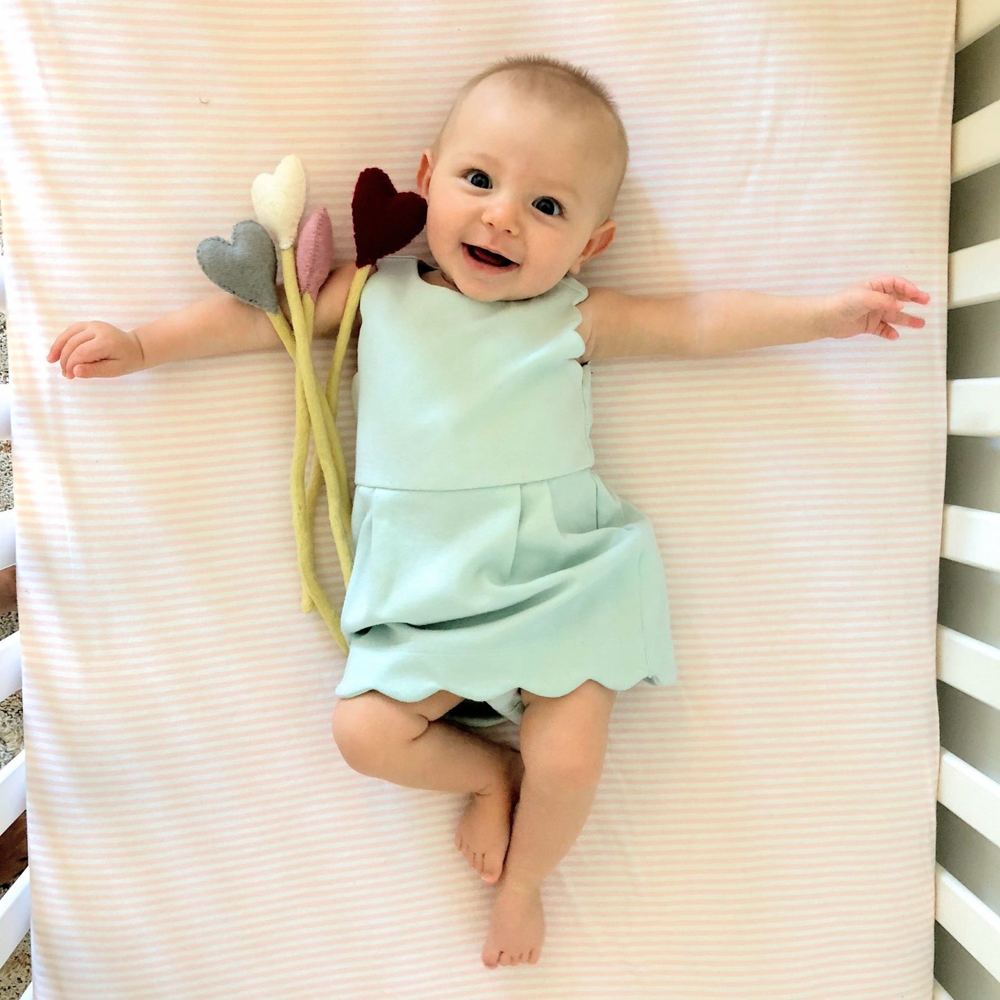 Felt heart accent stems in white, pink, blue, and red shown being held by baby in blue dress.