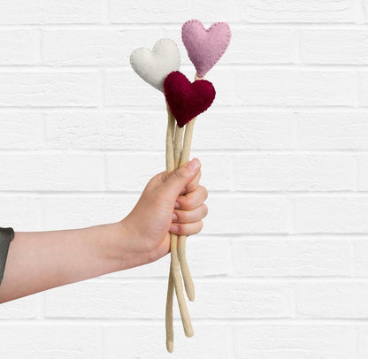 Felt heart accent stems in white, pink, and red shown being held out by a hand.