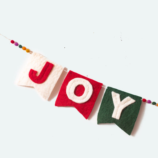 Close up of Joy from a felt garland spelling out Joy to the World in red and white letters on small dovetail flags in white, red, and green.