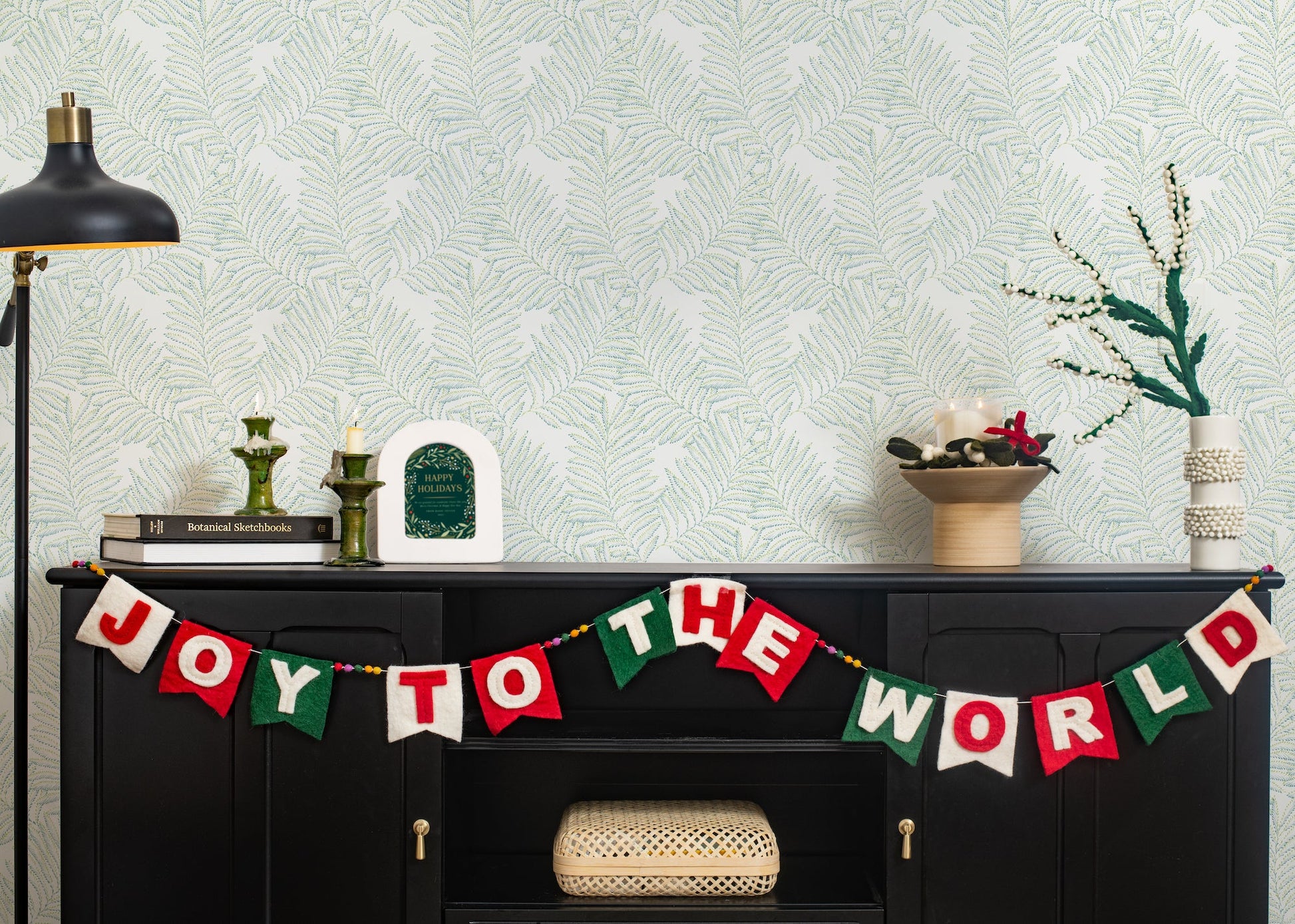 Felt garland spelling out Joy to the World in red and white letters on small dovetail flags in white, red, and green hanging on black cabinet.