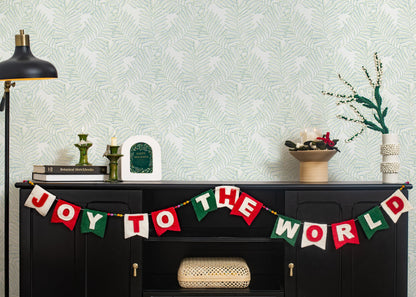 Felt garland spelling out Joy to the World in red and white letters on small dovetail flags in white, red, and green hanging on black cabinet.