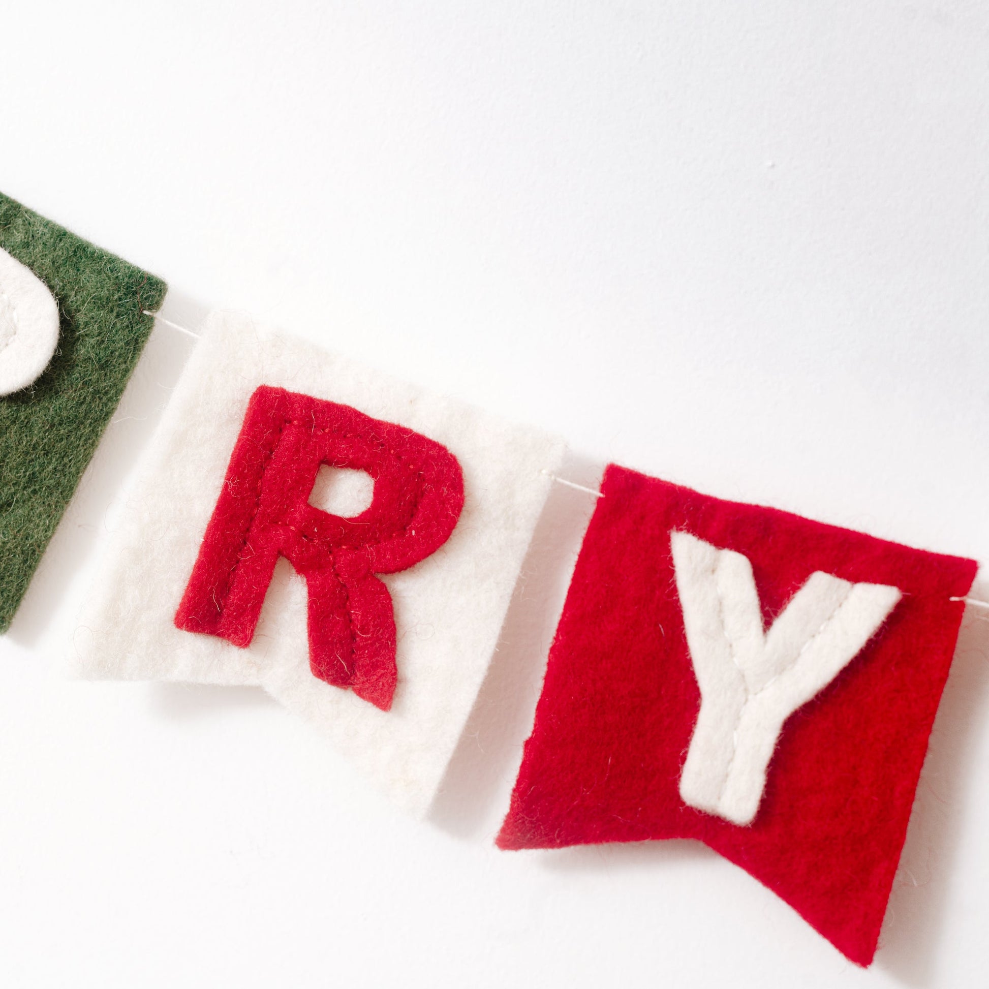 Close up of a red "R" on white flag and a white "Y" on red flag from a felt garland spelling out Merry Christmas in red and white letters on small dovetail flags in white, red, and green.