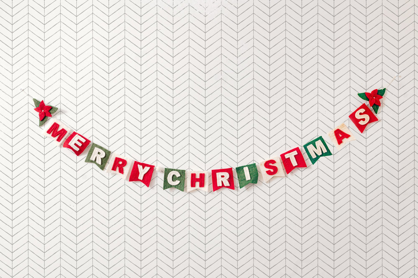 Felt garland spelling out Merry Christmas in red and white letters on small dovetail flags in white, red, and green.