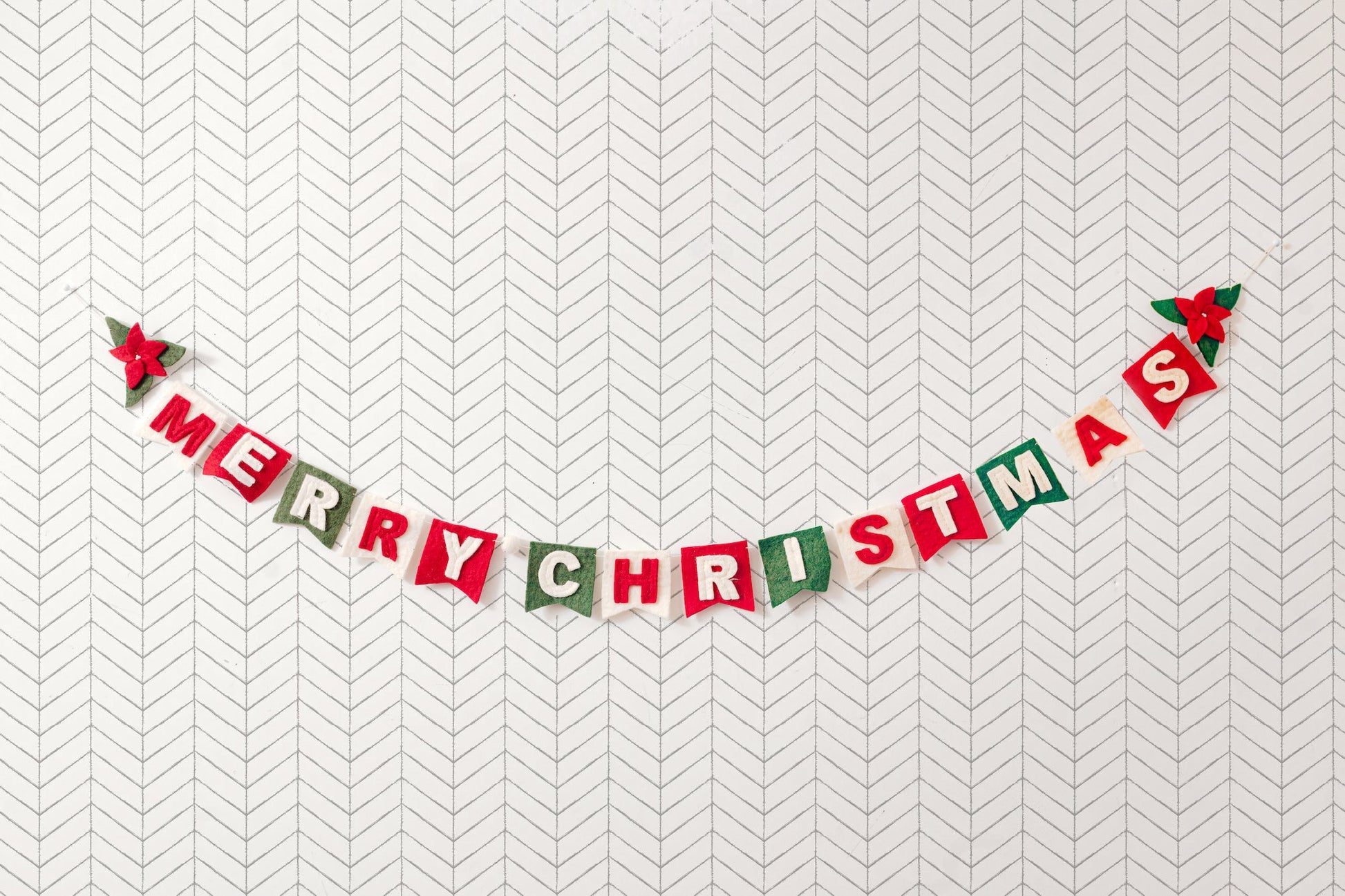 Felt garland spelling out Merry Christmas in red and white letters on small dovetail flags in white, red, and green.