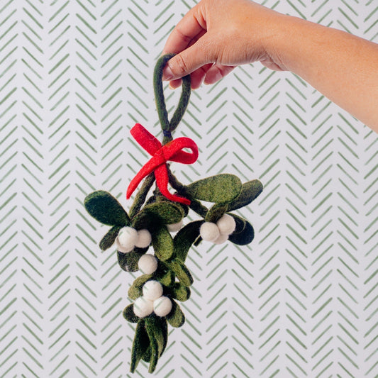 Hand holding a felt mistletoe ornament with green leaves, white berries, and a red bow.