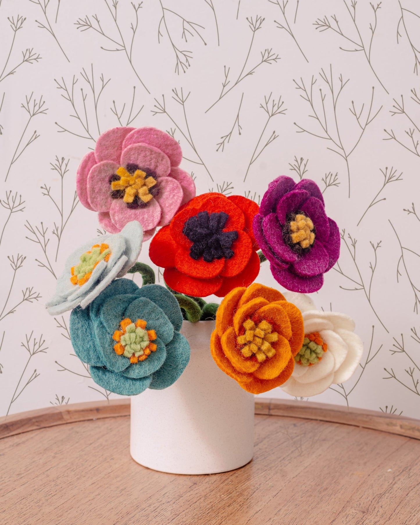 Felt poppy flowers in blue, light blue, pink, red, orange, purple and white in a white vase.