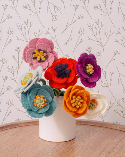 Felt poppy flowers in blue, light blue, pink, red, orange, purple and white in a white vase.