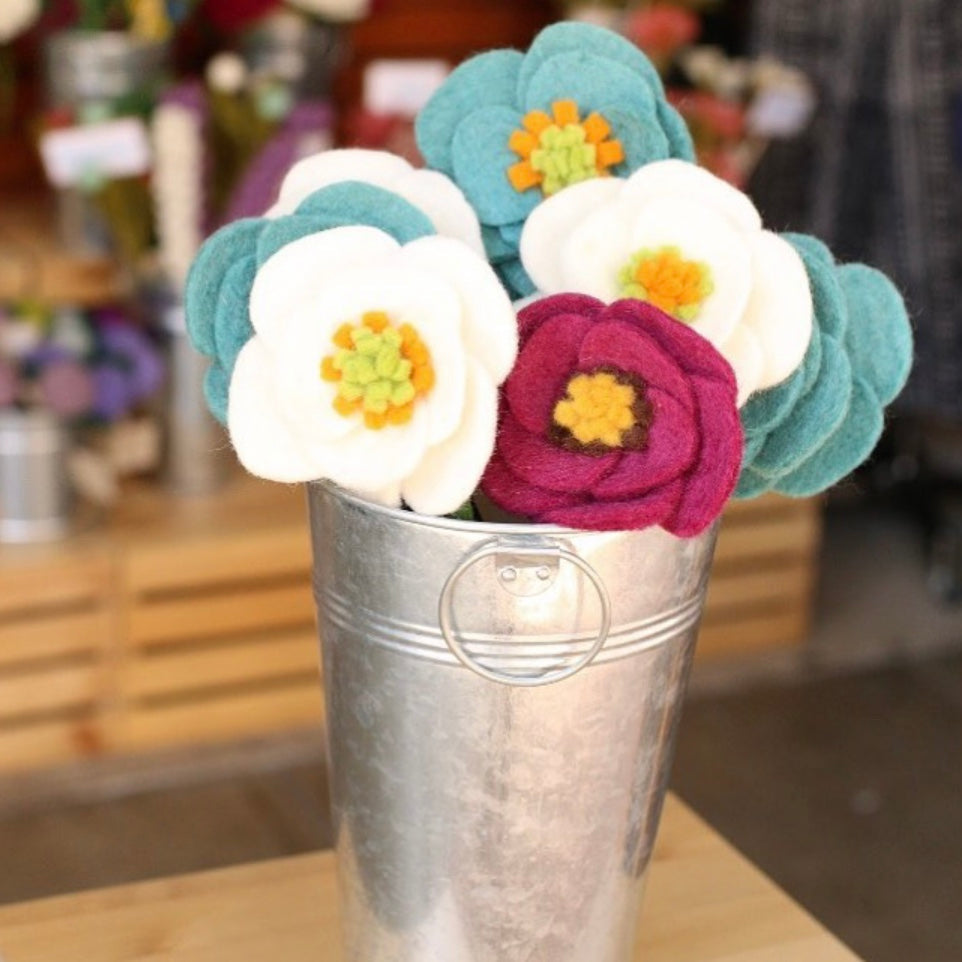 Metal bucket of blue, white, and magenta felt poppy flowers.