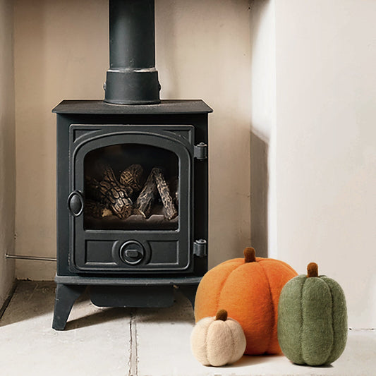Three felt pumpkins, one large orange pumpkin, one medium oblong green one, and one small tan one in front of fireplace.