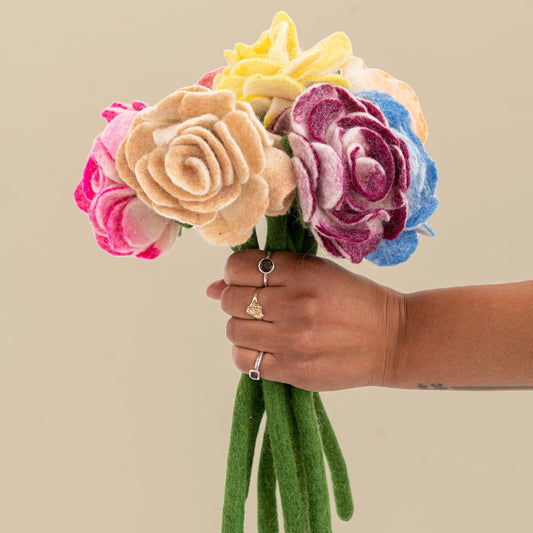 Bunch of felt ranunculus flowers in pink, cream, yellow, blue, purple being held in a hand reaching out.