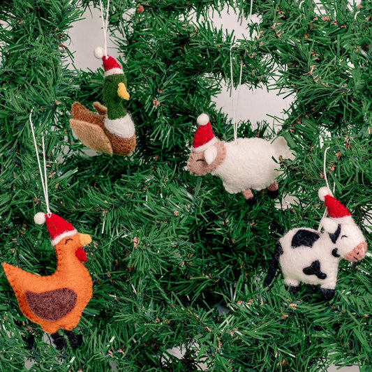 Felt ornaments of a duck, a chicken, a cow, and a sheep in Santa hats hanging on a Christmas tree.