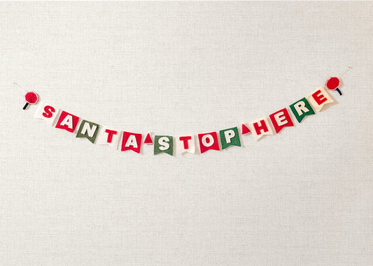 Felt garland spelling out Santa Stop Here in red and white letters on small dovetail flags in white, red, and green.