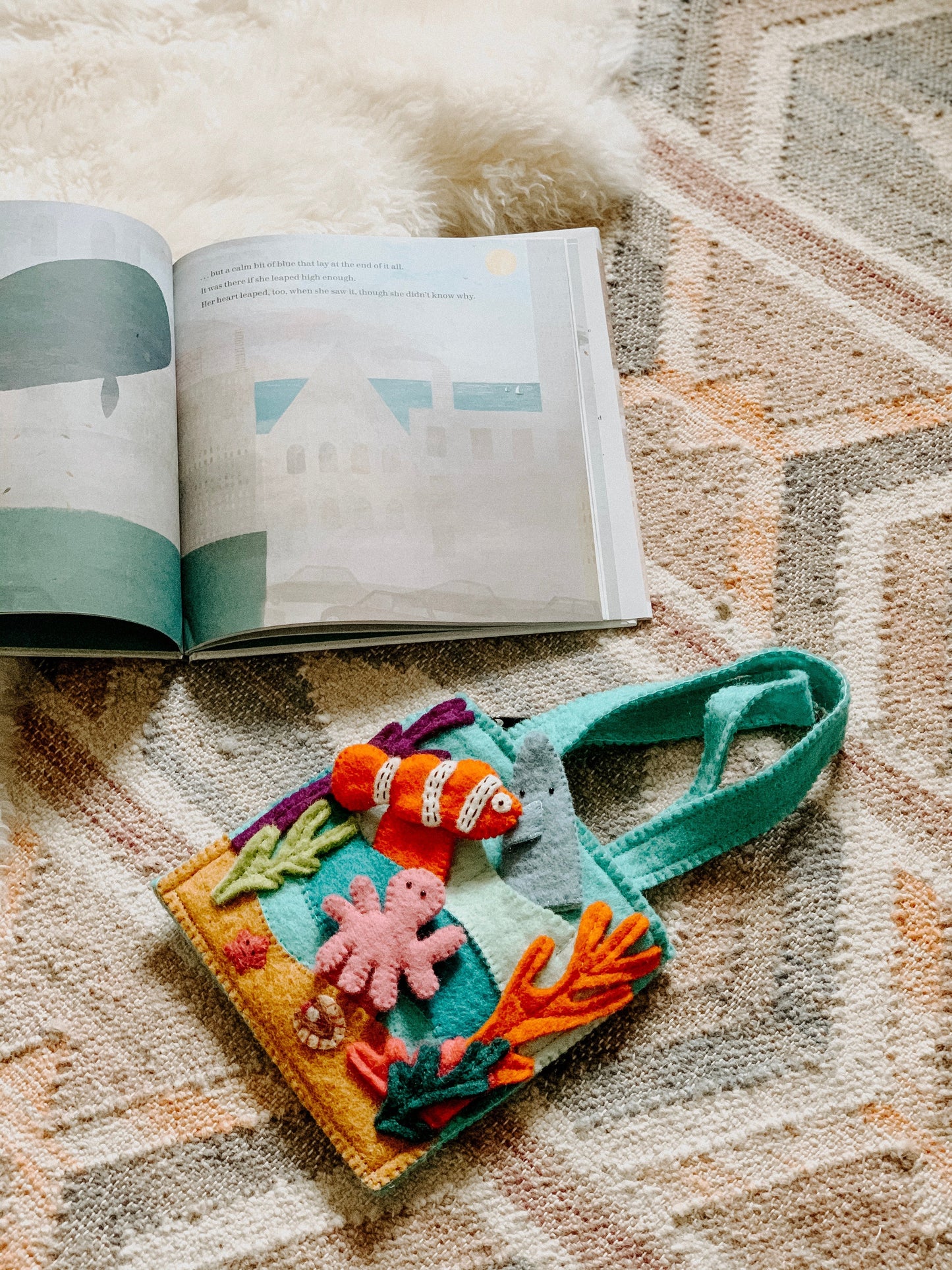 Felt bag with under the sea finger puppets of an orange and white clown fish, a pink octopus, and a grey shark laying on a rug.