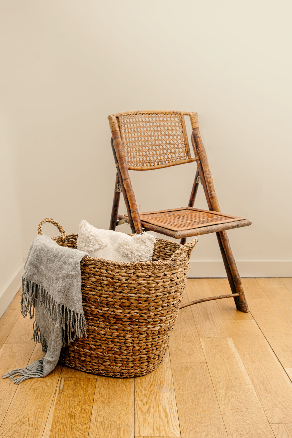 Brown large woven basket holding blankets, next to a chair.