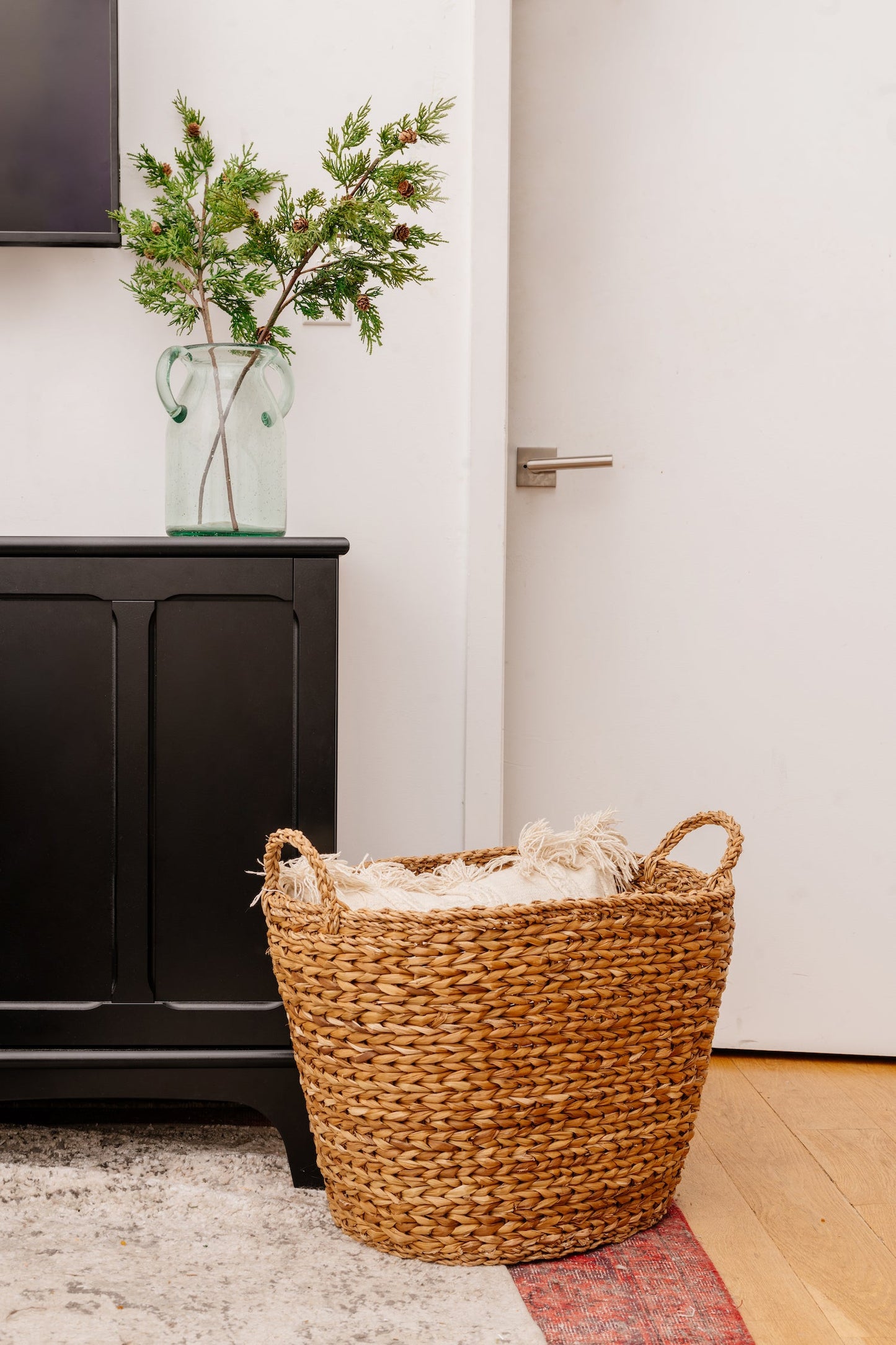 Brown large woven basket on rug next to black cabinet.